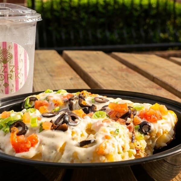 Loaded fries with cheese sauce, tomatoes, olives, and green onions, next to a Fizz & Fork drink.